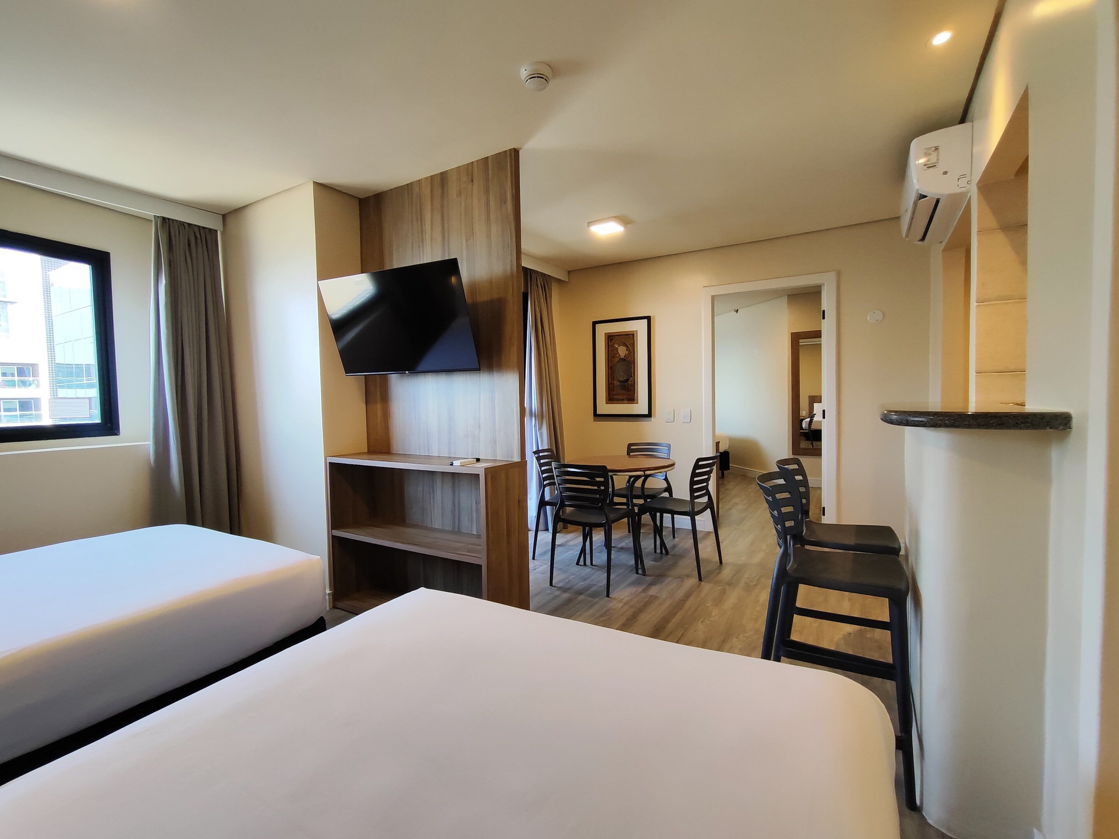A hotel room with two beds, a TV mounted on the wall, a dining area with chairs, and a small table.