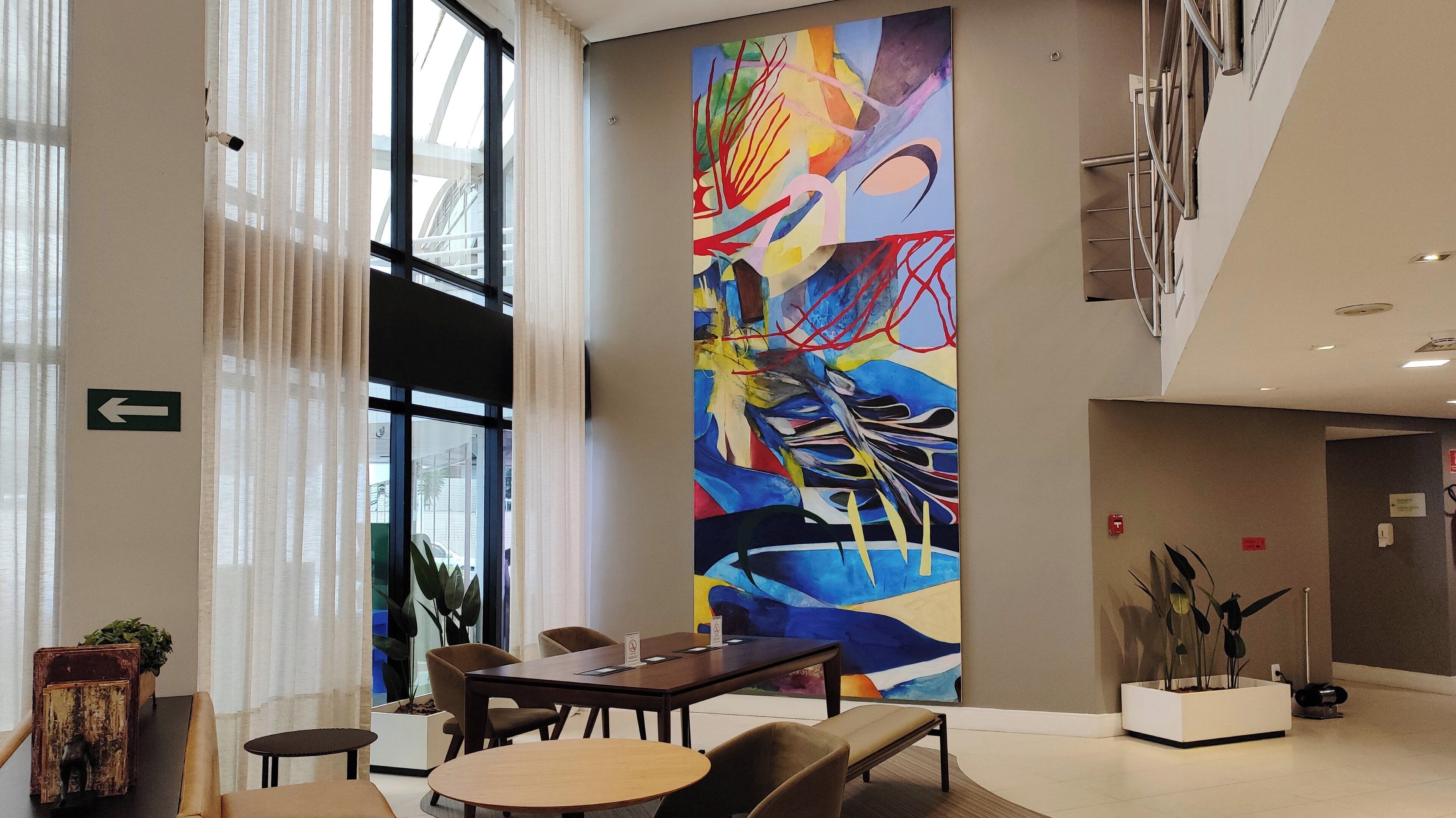 A modern lobby with a large abstract painting, a reception desk, seating area, and a staircase.