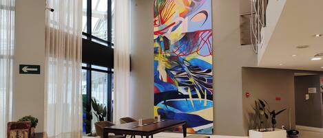 A modern lobby with a large abstract painting, a reception desk, seating area, and a staircase.