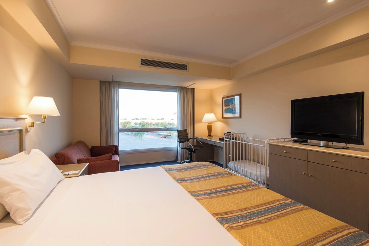 A hotel room with a large bed, a desk, a chair, a television, and a window with a view.