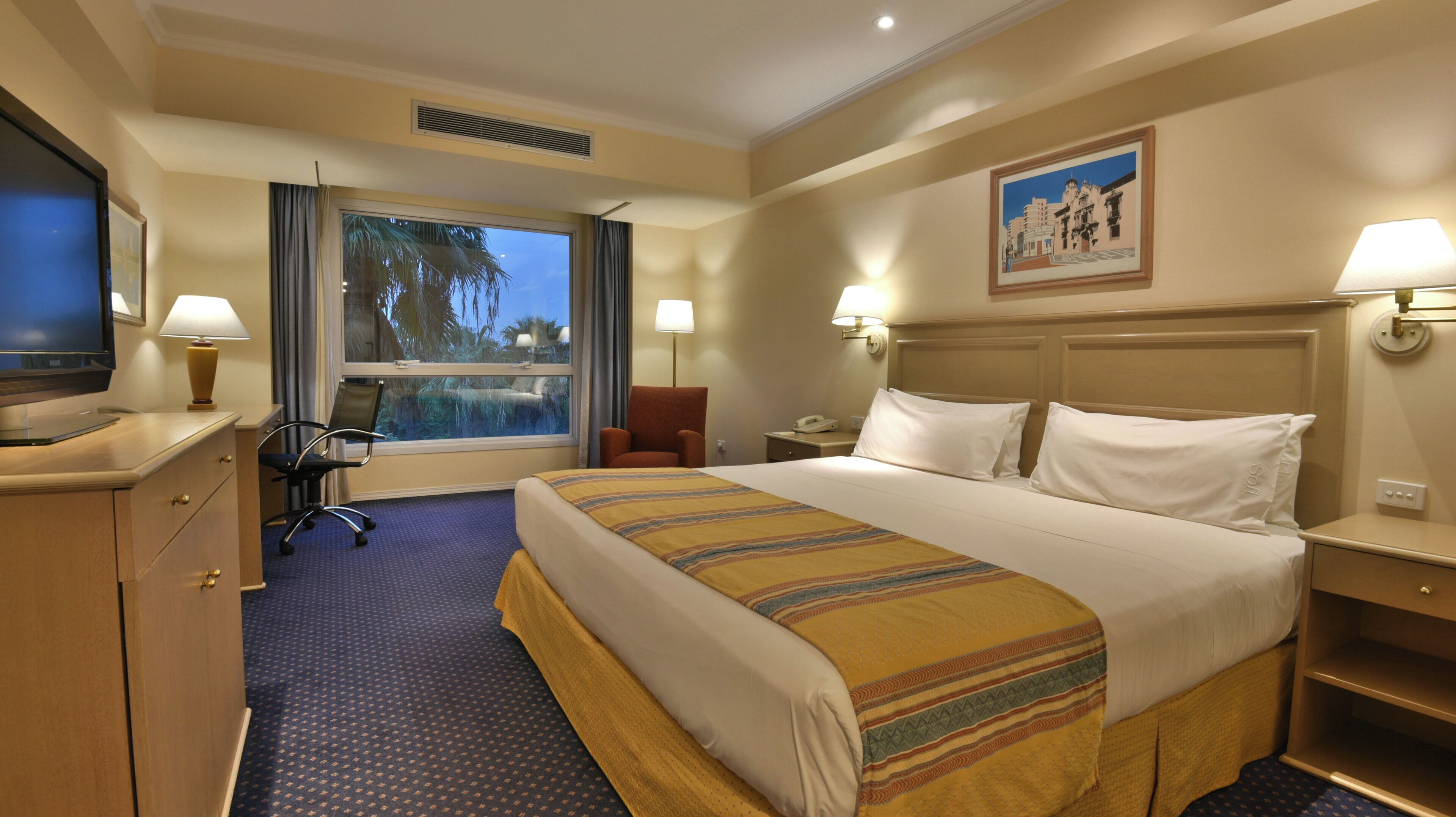 A hotel room with a bed, desk, chair, TV, and a window with a view.