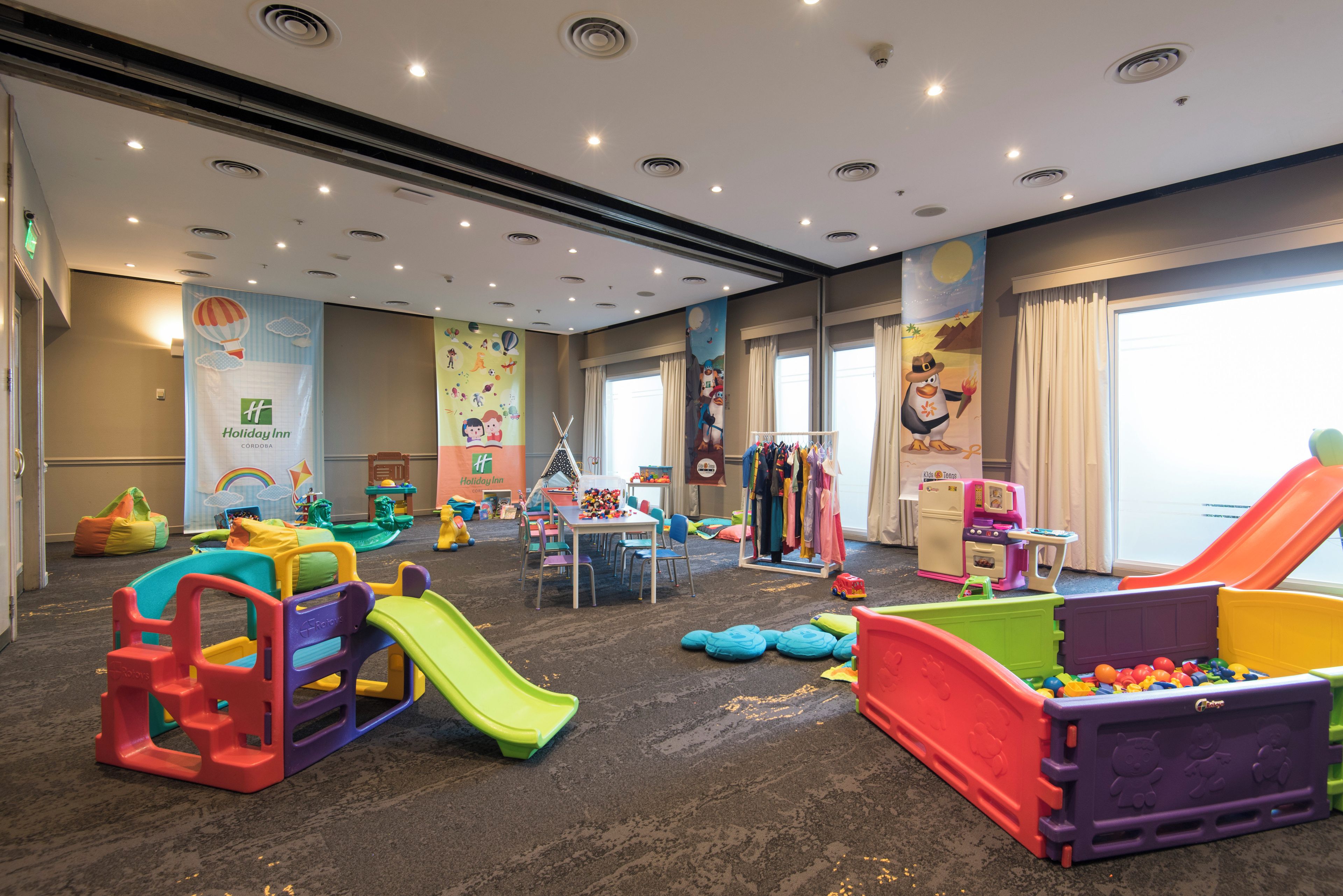 A children's play area with various play structures, including slides and climbing frames, and a wall decorated with colorful murals.
