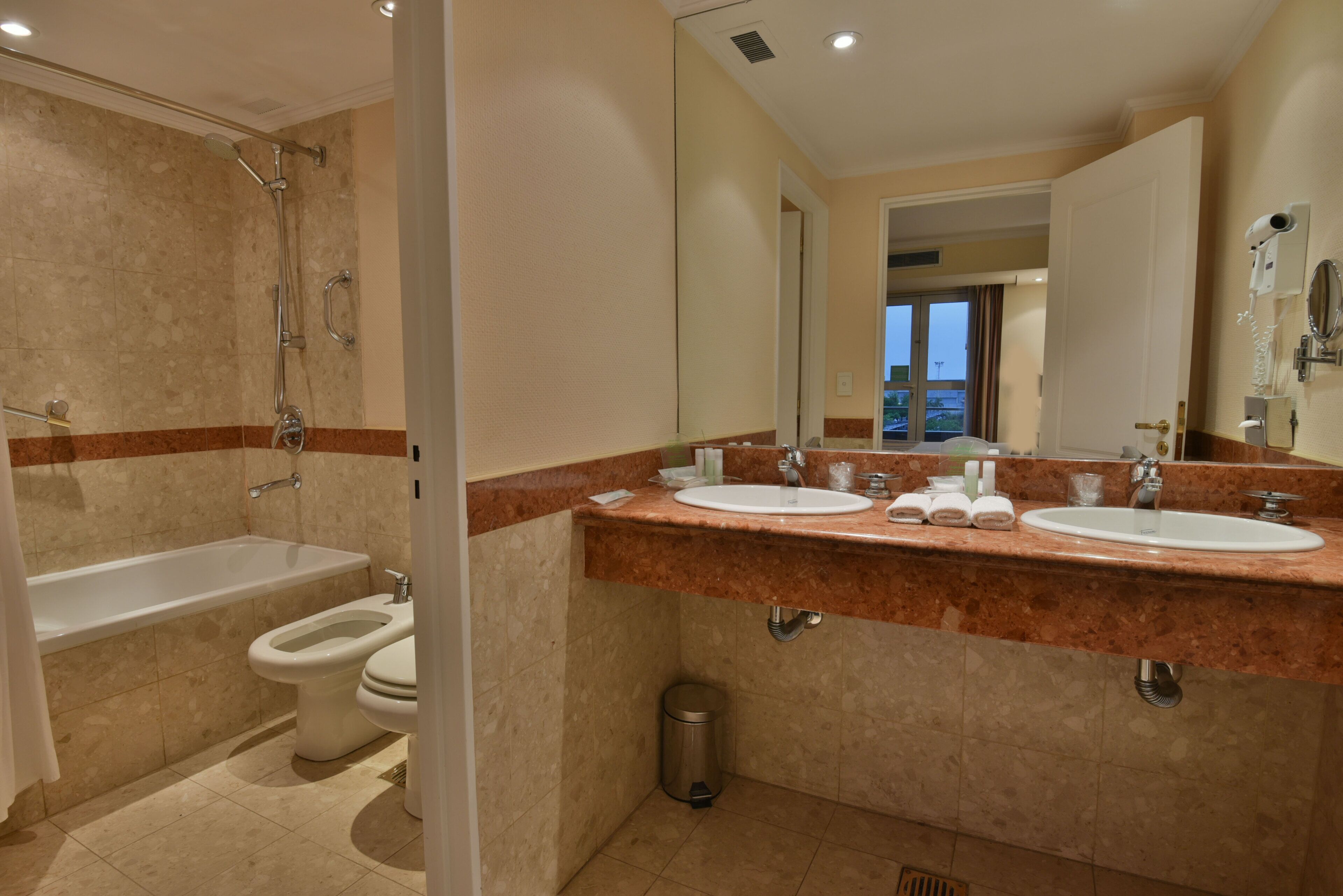 A bathroom with a bathtub, two sinks, a toilet, and a trash can.