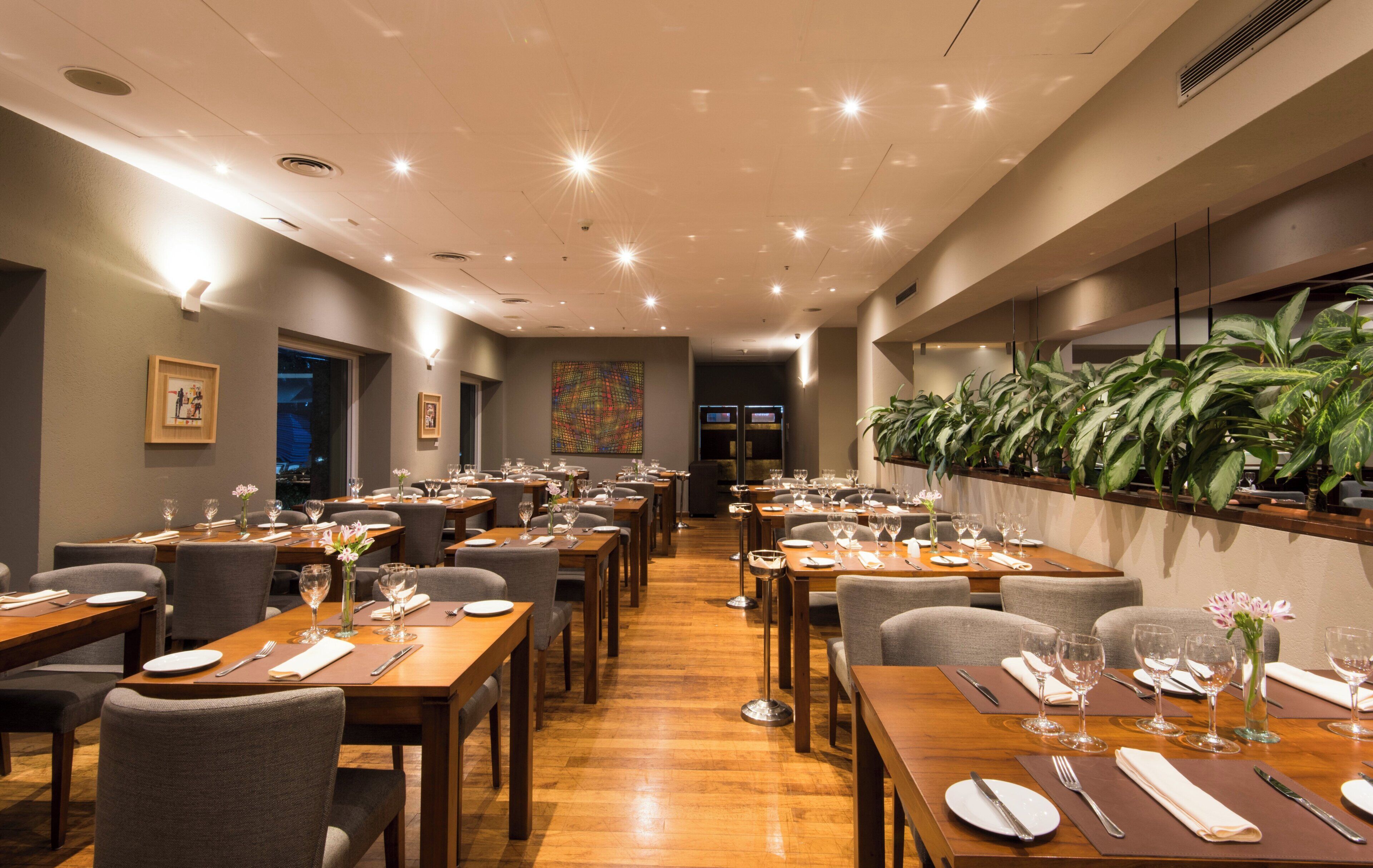 Un restaurante con varias mesas, sillas y una variedad de plantas en las paredes.