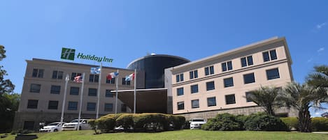 A Holiday Inn hotel with multiple flags, a parking lot, and a well-maintained lawn.