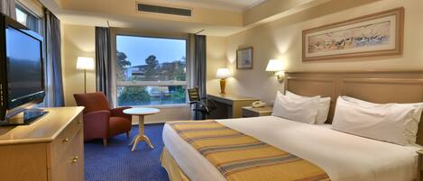 A hotel room with a bed, a desk, a chair, a TV, and a window with a view.