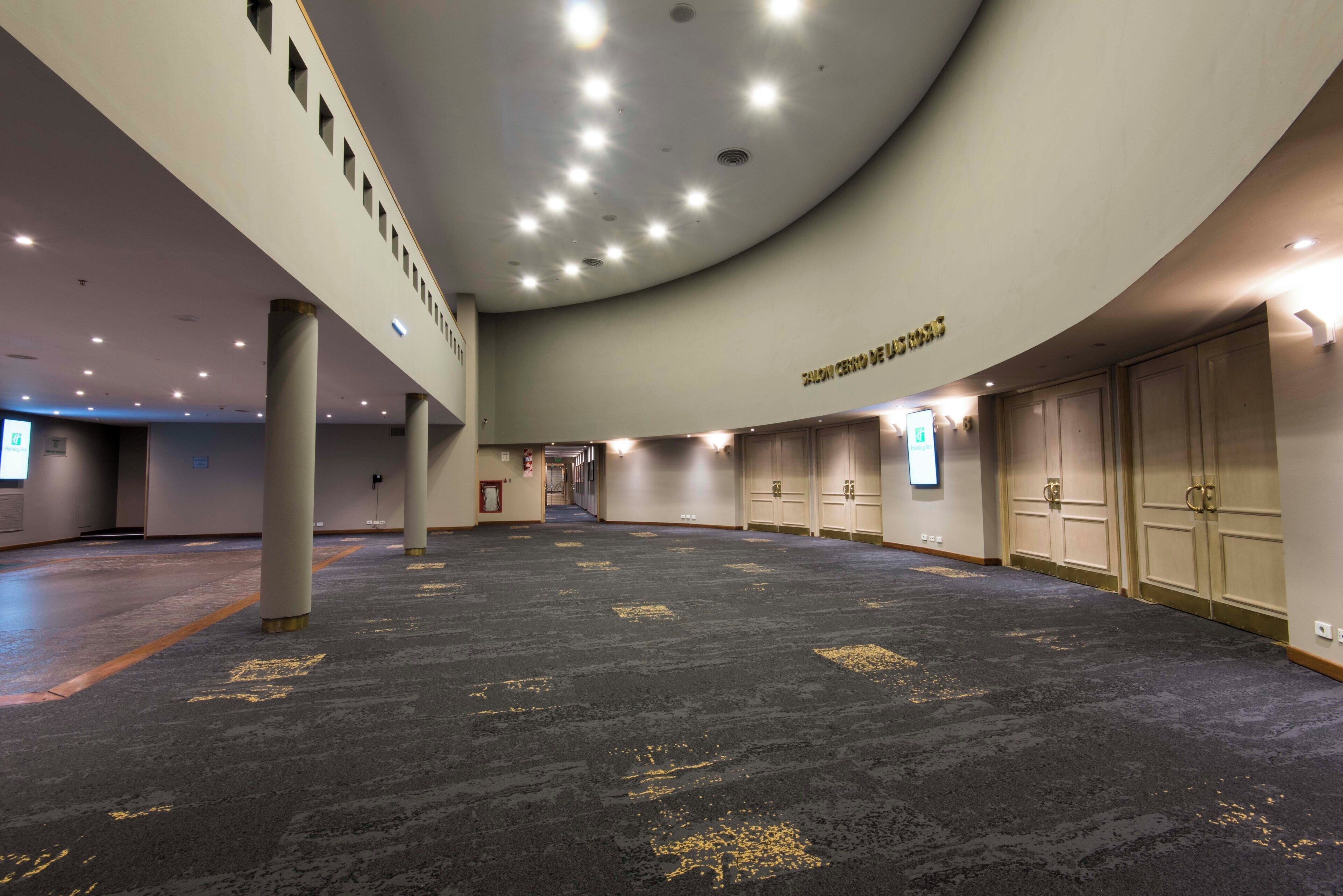 A spacious indoor area with a curved ceiling, multiple columns, and a carpeted floor with directional markings.