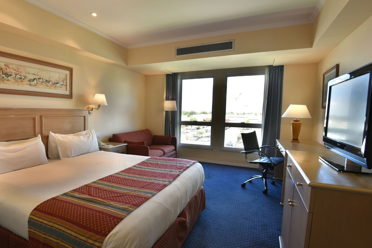 Habitación de hotel con una cama grande, un escritorio con televisor de pantalla plana, una silla, una lámpara de escritorio y una ventana con vistas.