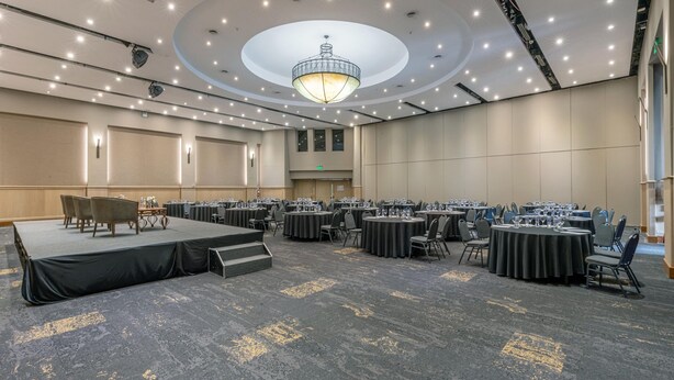 Uma sala de conferências ampla com várias mesas redondas, um palco e um candelabro.