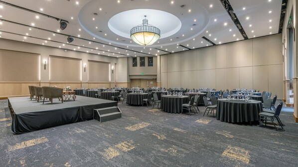 A large conference room with multiple round tables, a stage, and a chandelier. - Holiday Inn Córdoba by IHG (Córdoba)