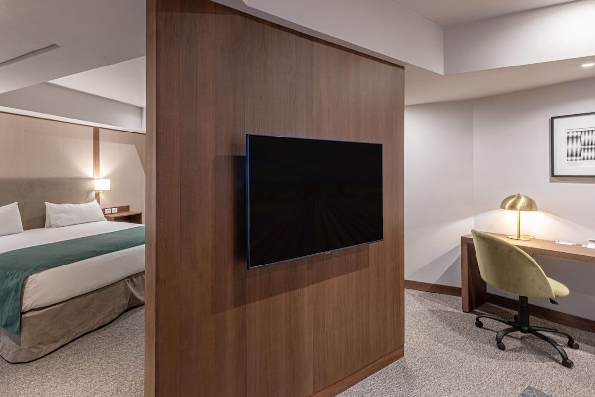 Una habitación de hotel con cama, escritorio, silla, televisión y lámpara.