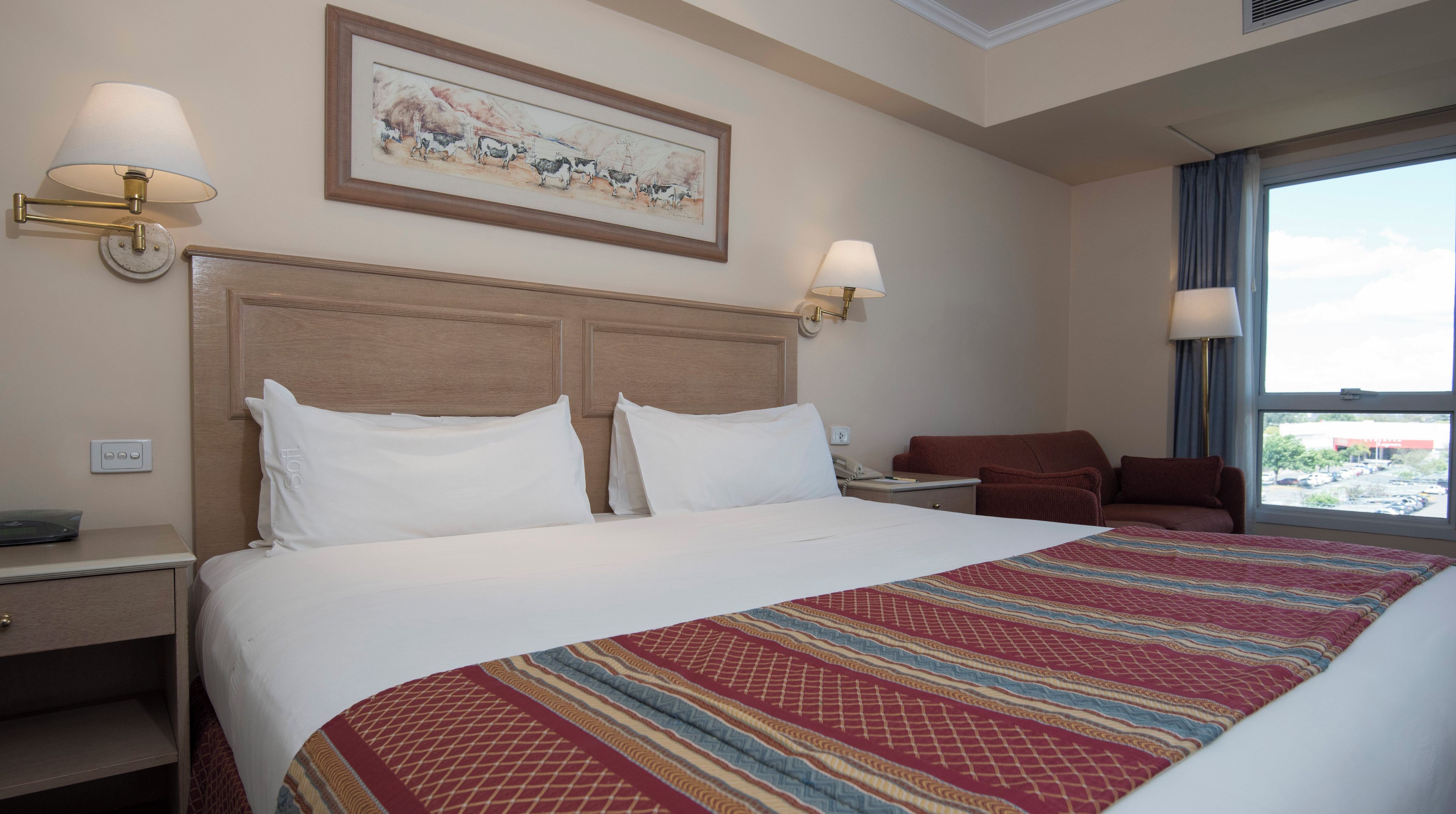 Hotelkamer met een groot bed, twee nachtkastjes, een bureau, een stoel, een raam met uitzicht en wandlampen.