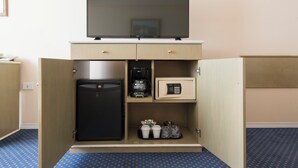 Quarto de hotel com minibar, televisão, frigorífico, máquina de café e cofre.