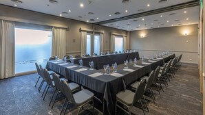 Uma sala de conferência com uma mesa comprida, cadeiras, garrafas de água e copos.