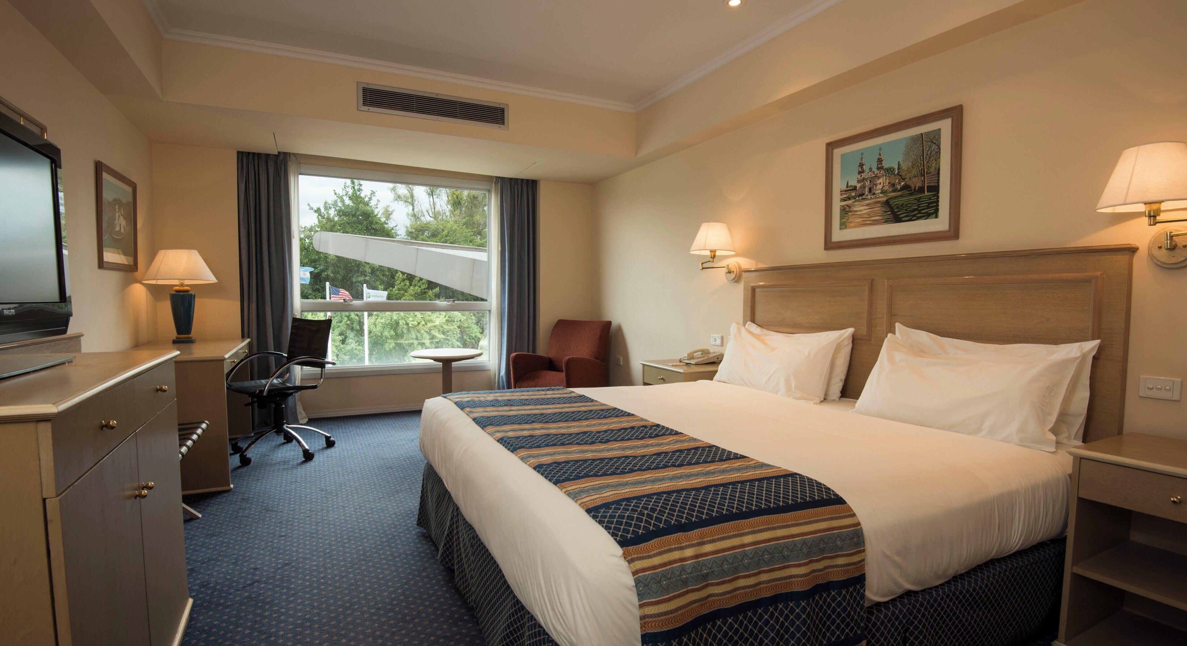 A hotel room with a bed, desk, chair, and a window with a view.