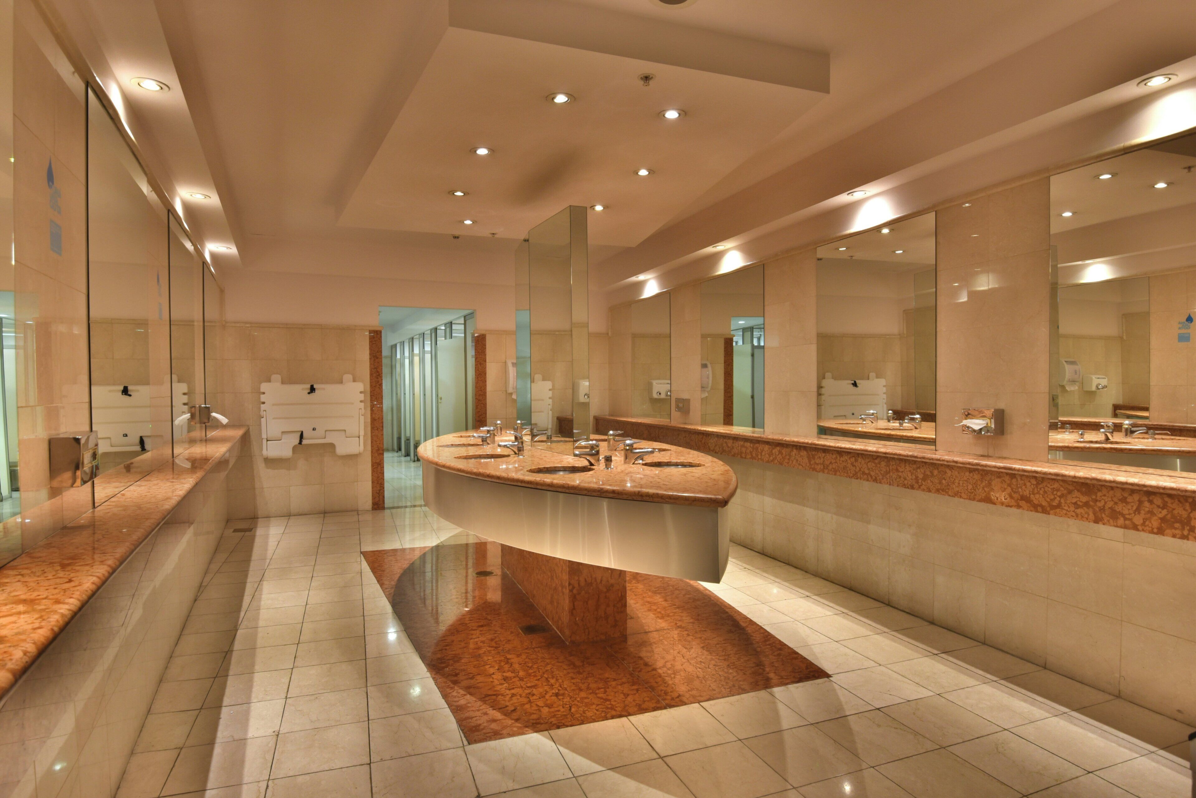 Un baño moderno con un lavamanos central en isla, varios espejos y suelo de baldosas.