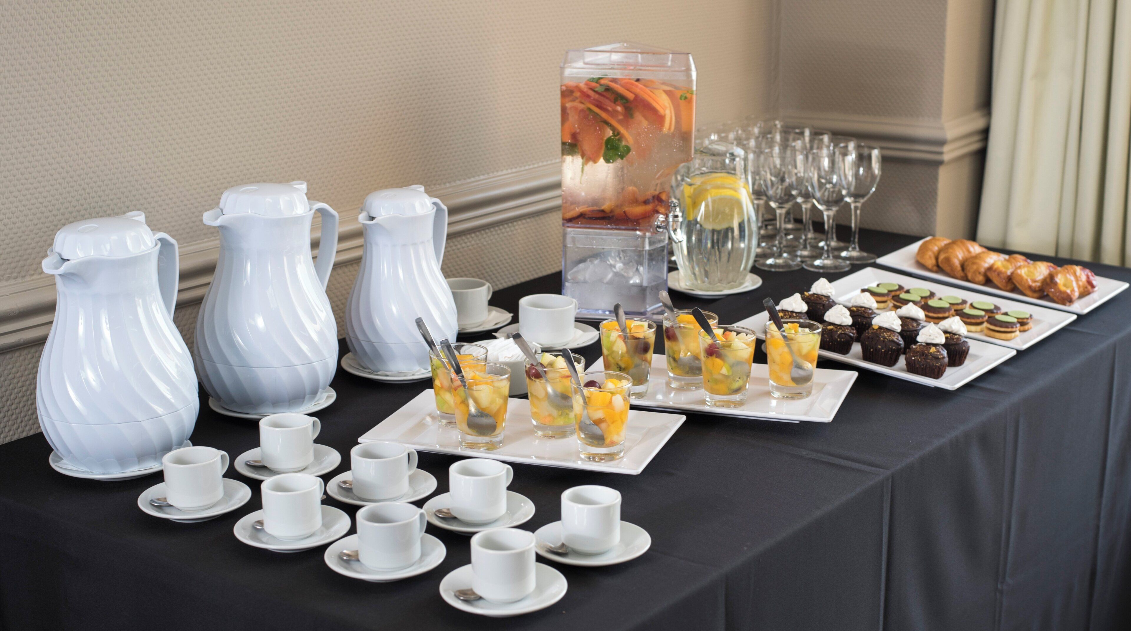 A buffet table with various food items, including fruit cups, pastries, and a pitcher of iced tea.