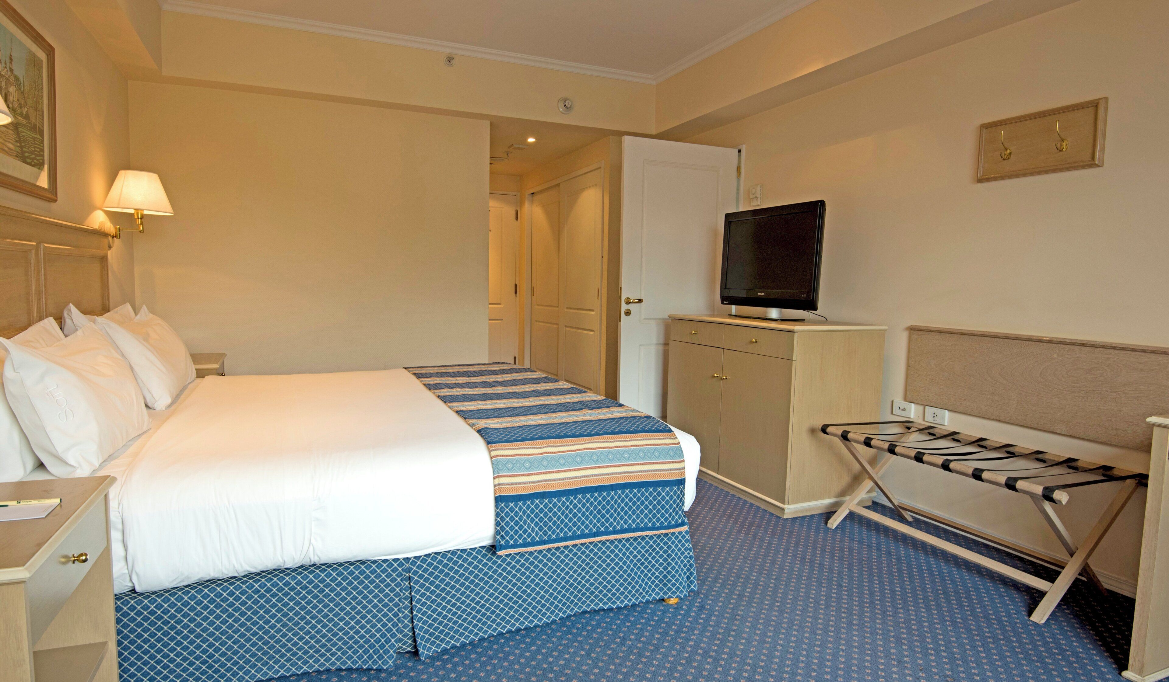 A hotel room with a bed, a television on a stand, a wardrobe, and an ironing board.
