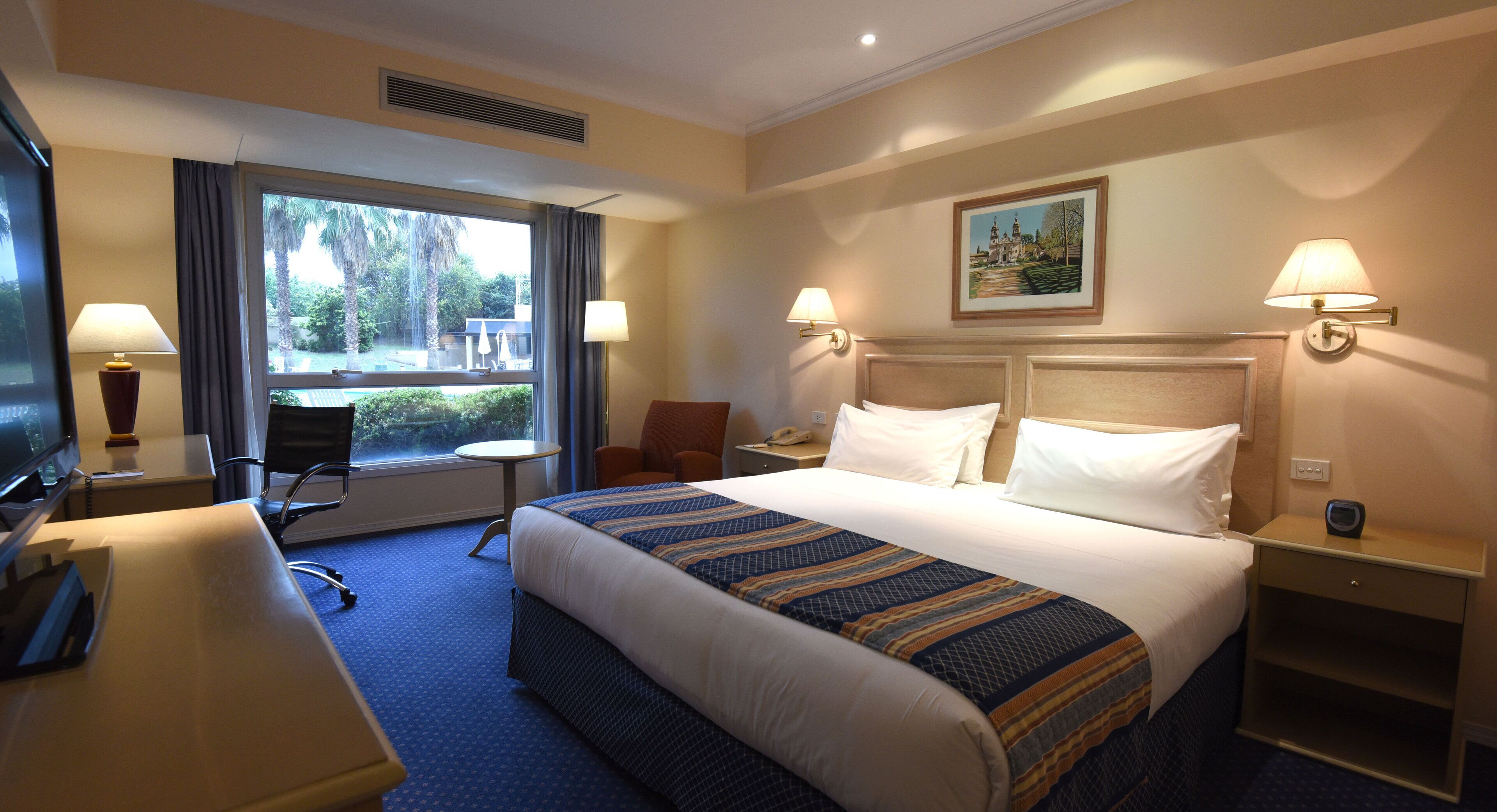 A hotel room with a large bed, a desk, a chair, a TV, and a window with curtains.
