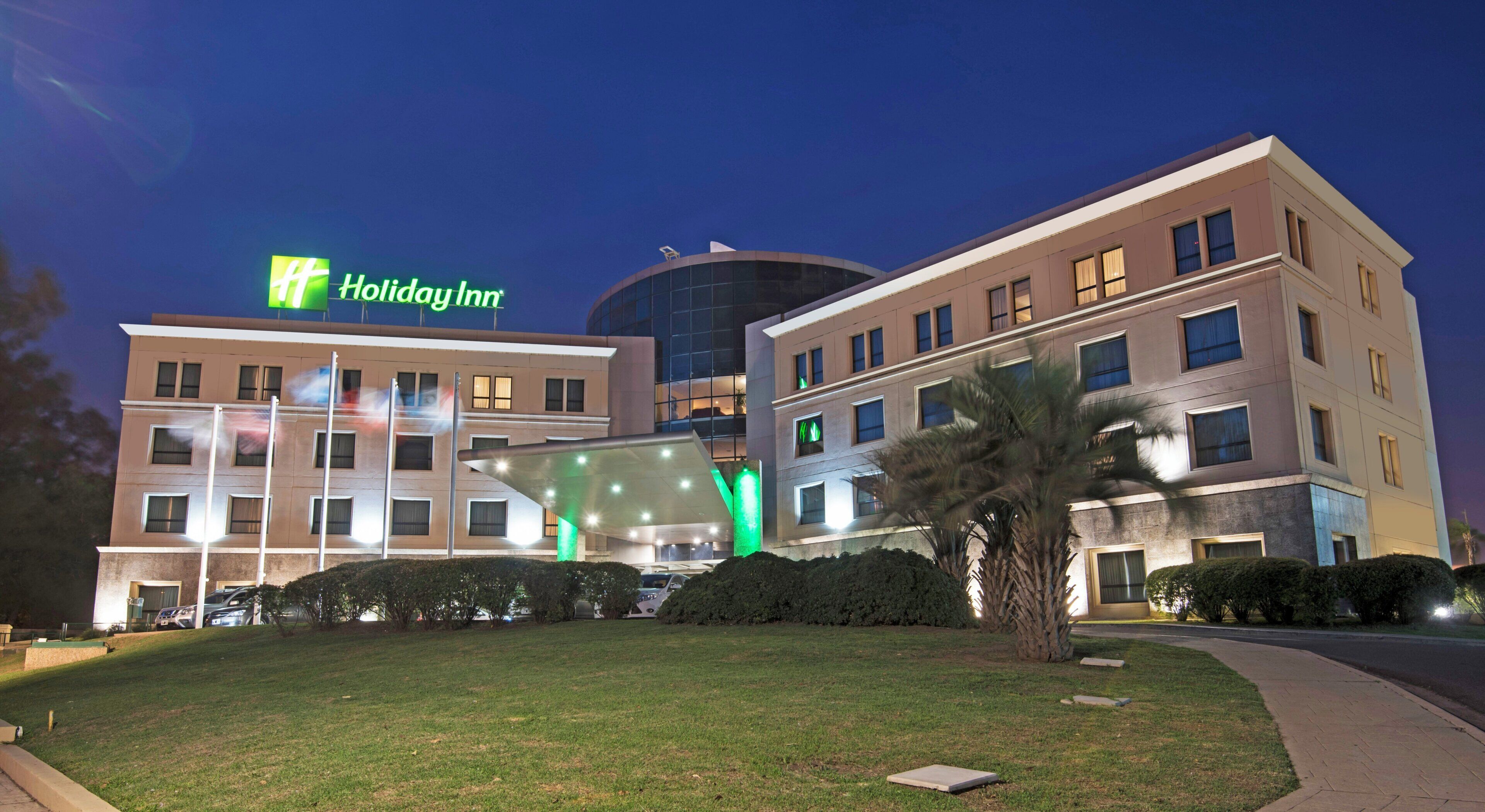A Holiday Inn hotel with a modern design, featuring a prominent glass facade and a well-maintained lawn.