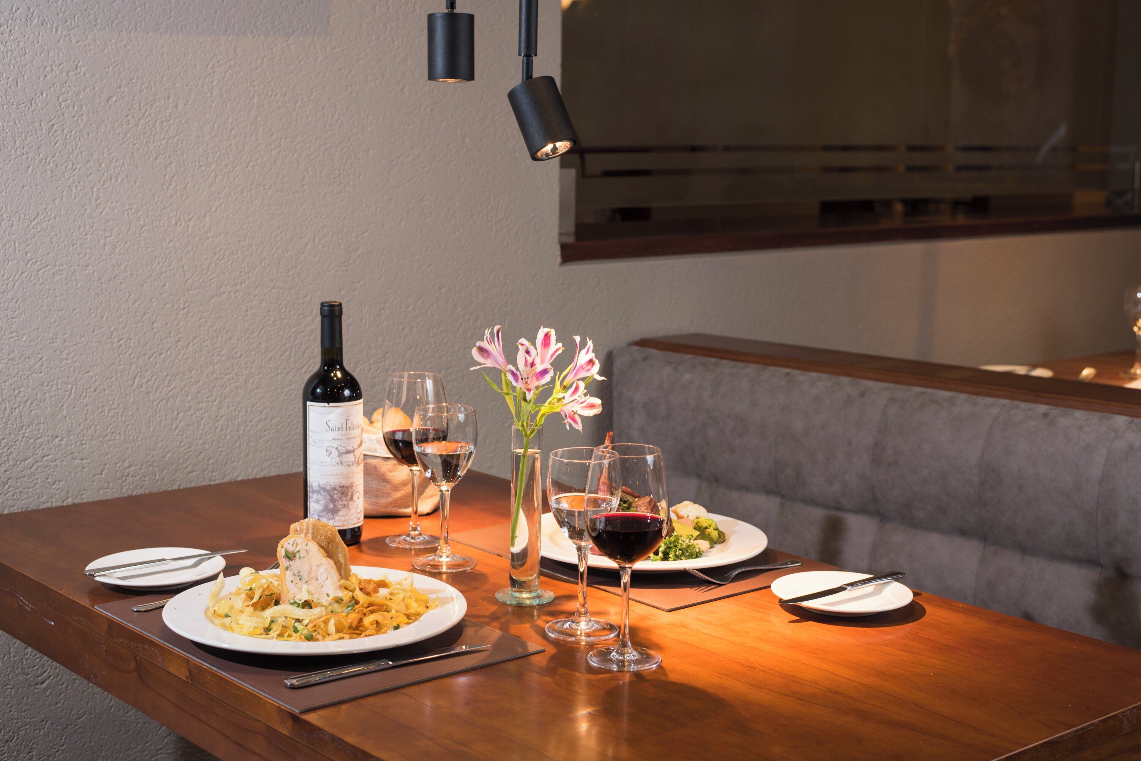 A dining table set with plates of food, wine glasses, a bottle of wine, and a vase with flowers.