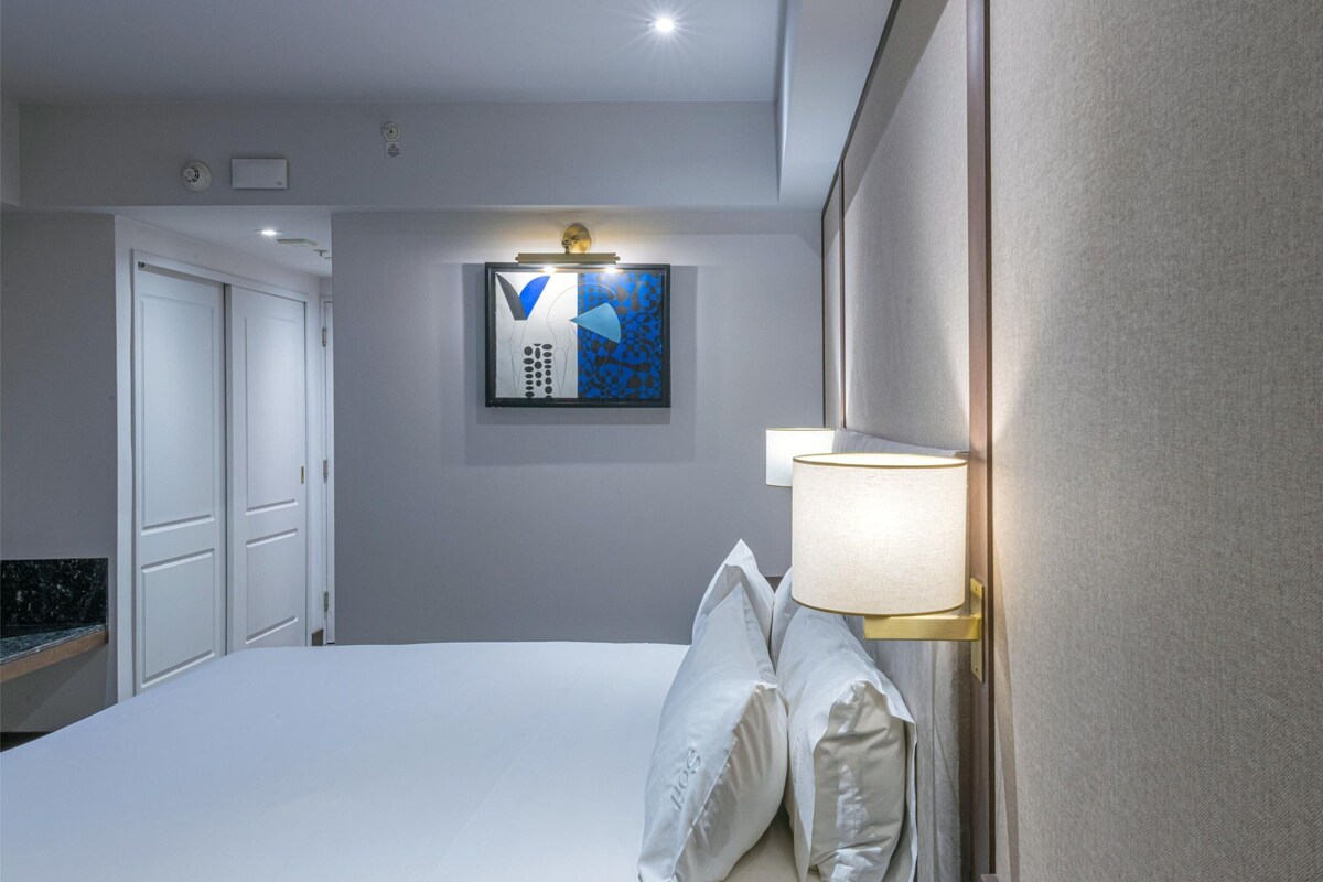 A hotel room with a bed, a wall-mounted lamp, and a painting on the wall.