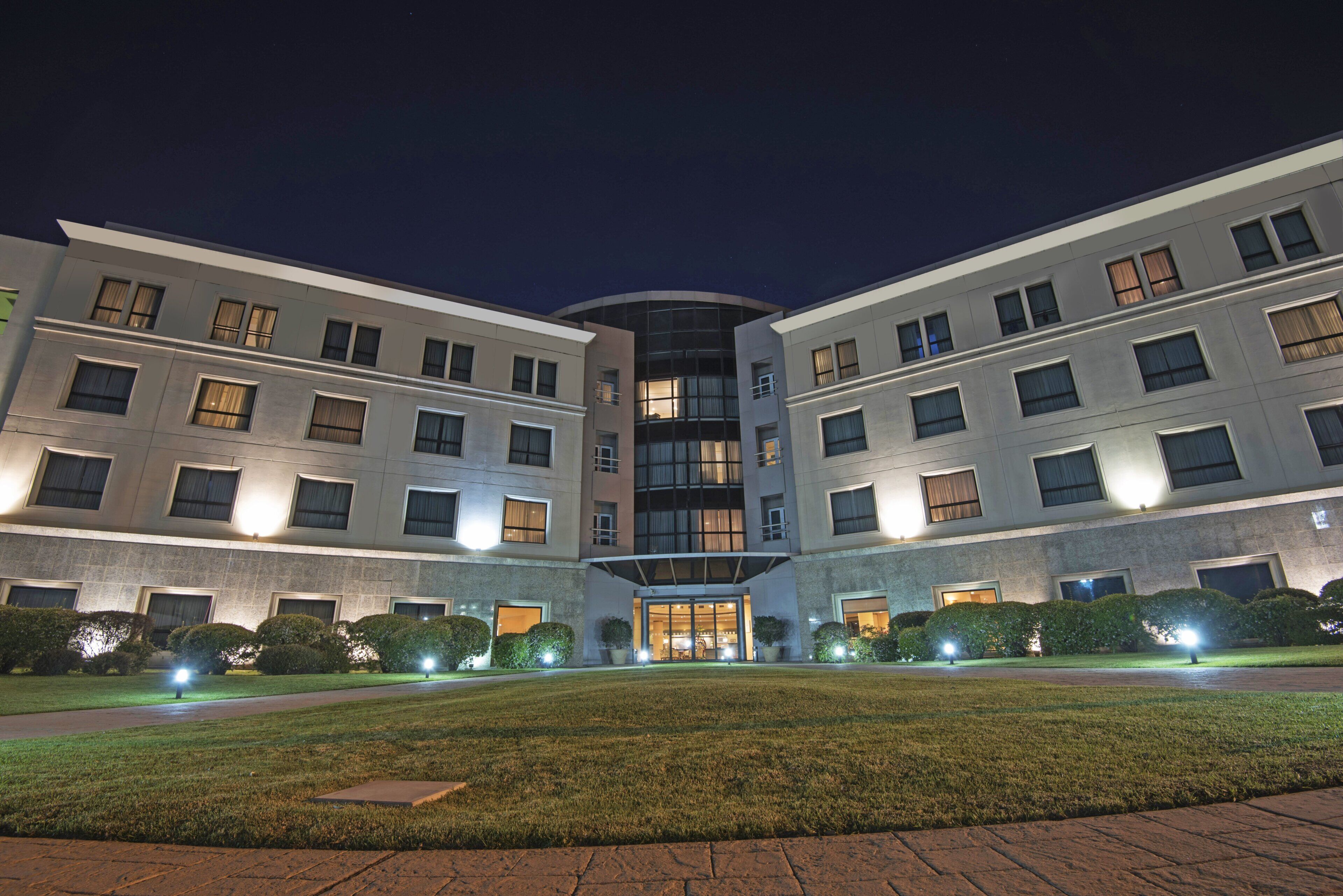 A multi-story hotel with a central entrance, surrounded by well-maintained lawns and hedges.