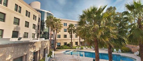 A hotel with a swimming pool, outdoor seating, and palm trees.