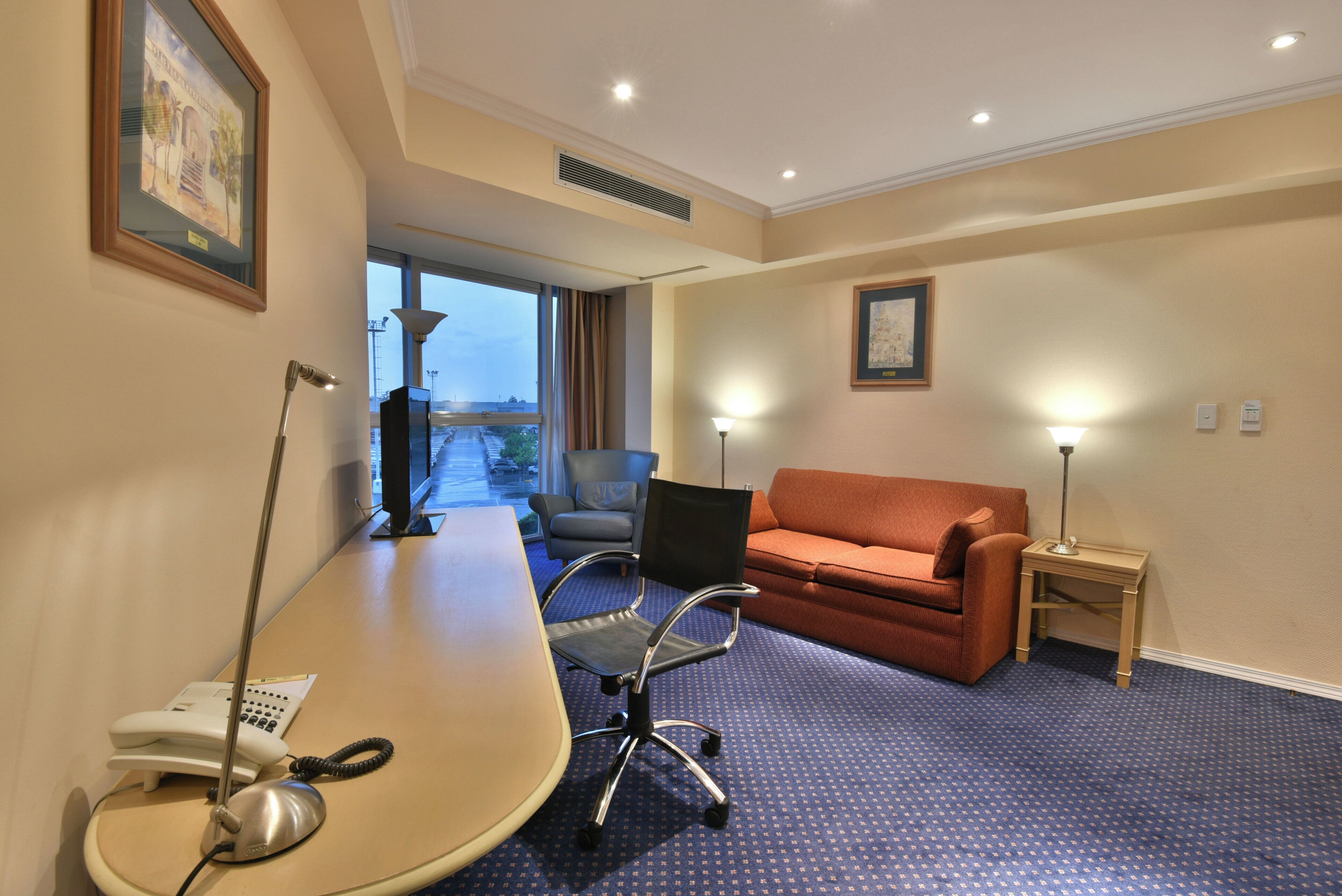 Habitación de hotel con escritorio, silla, sofá y vistas al exterior.