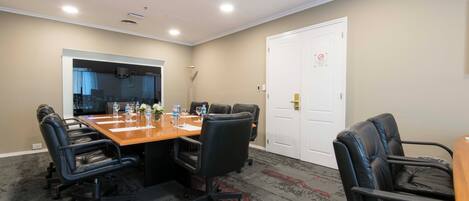 Sala de conferência com uma mesa comprida, cadeiras de couro preto e uma porta branca com placa de proibido fumar.