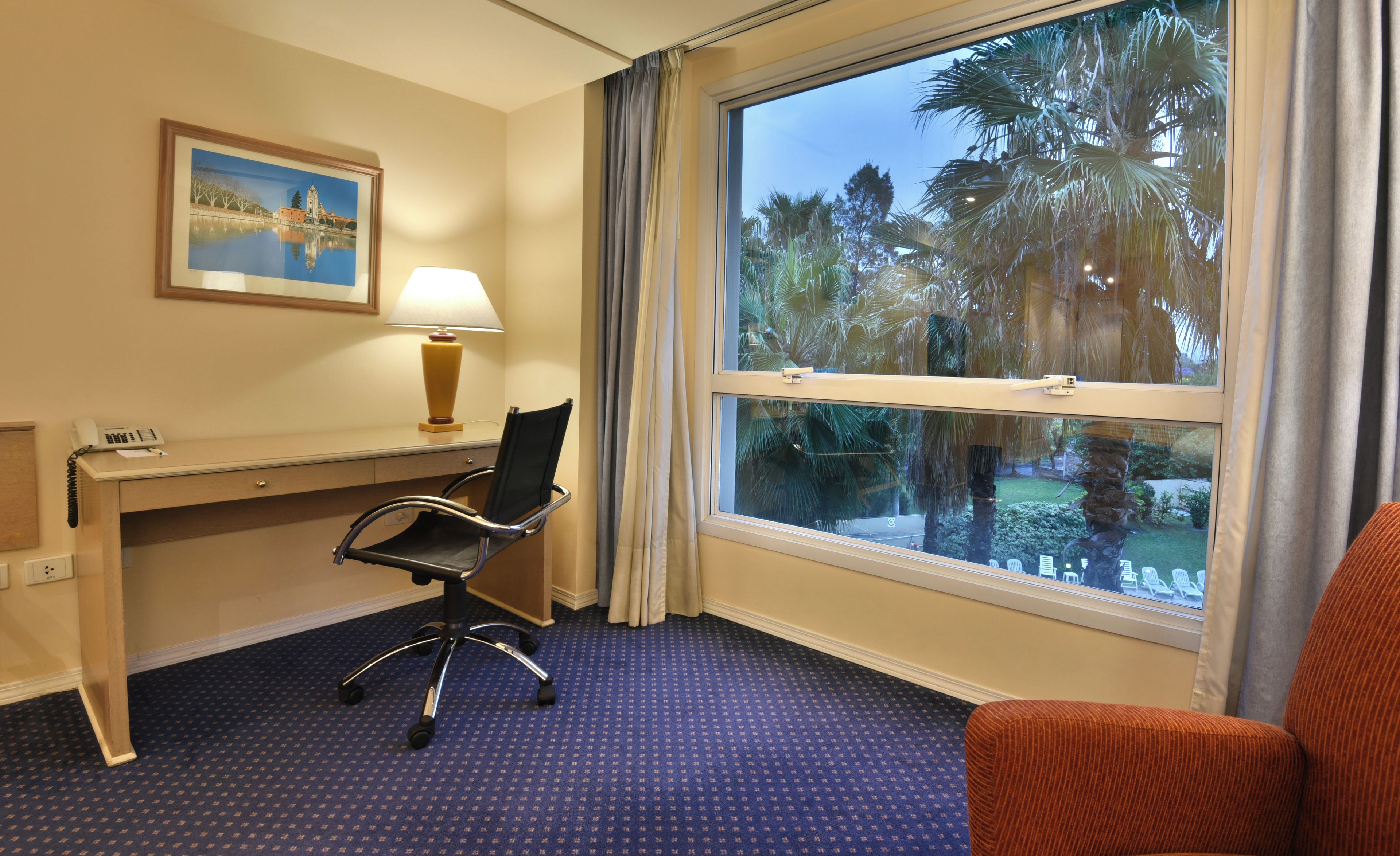 A hotel room with a desk, chair, and a large window with a view of palm trees.