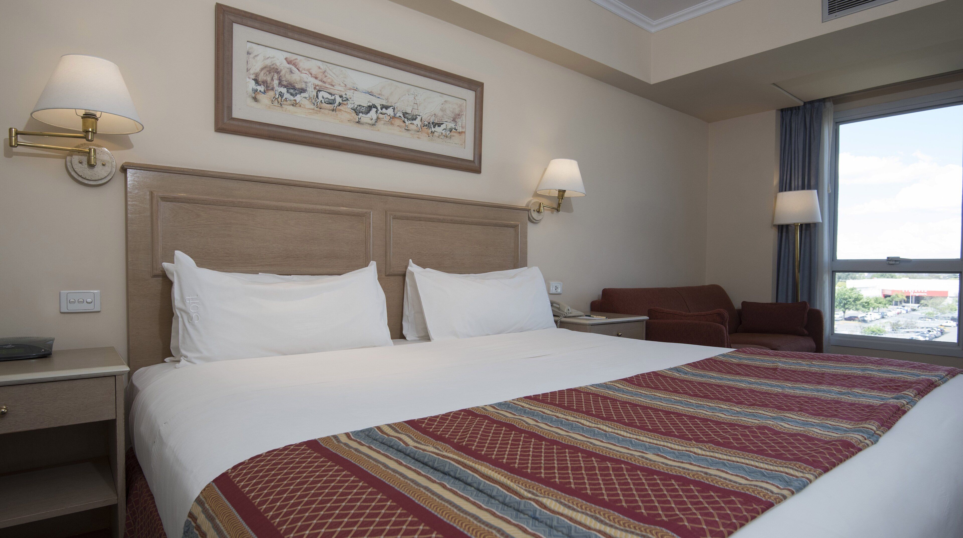 A hotel room with a large bed, two bedside tables, a nightstand, a desk, a chair, and a window with a view.