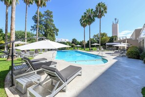 A swimming pool with lounge chairs and umbrellas, surrounded by palm trees and a building with a modern design. - Holiday Inn Córdoba by IHG (Córdoba)