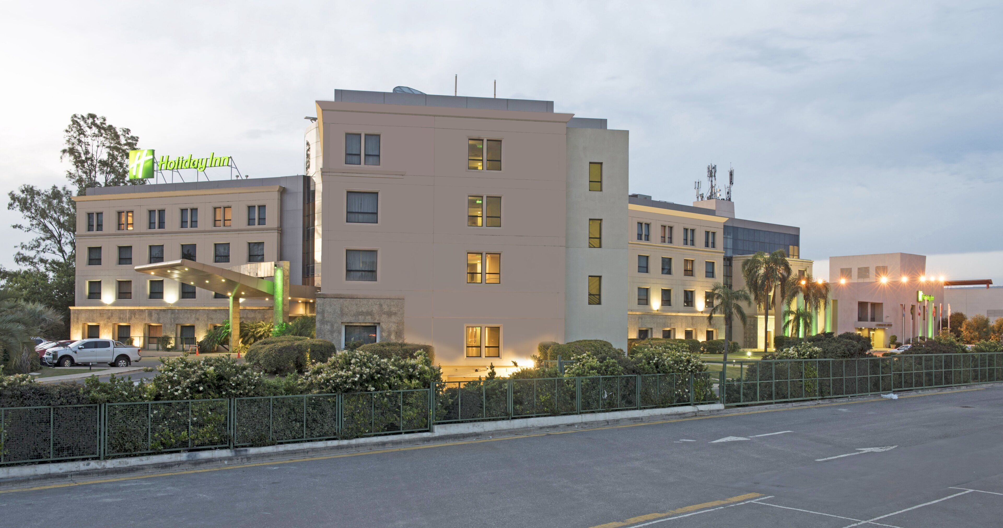 A multi-story hotel with a flat facade, multiple windows, and a parking area with a few cars.