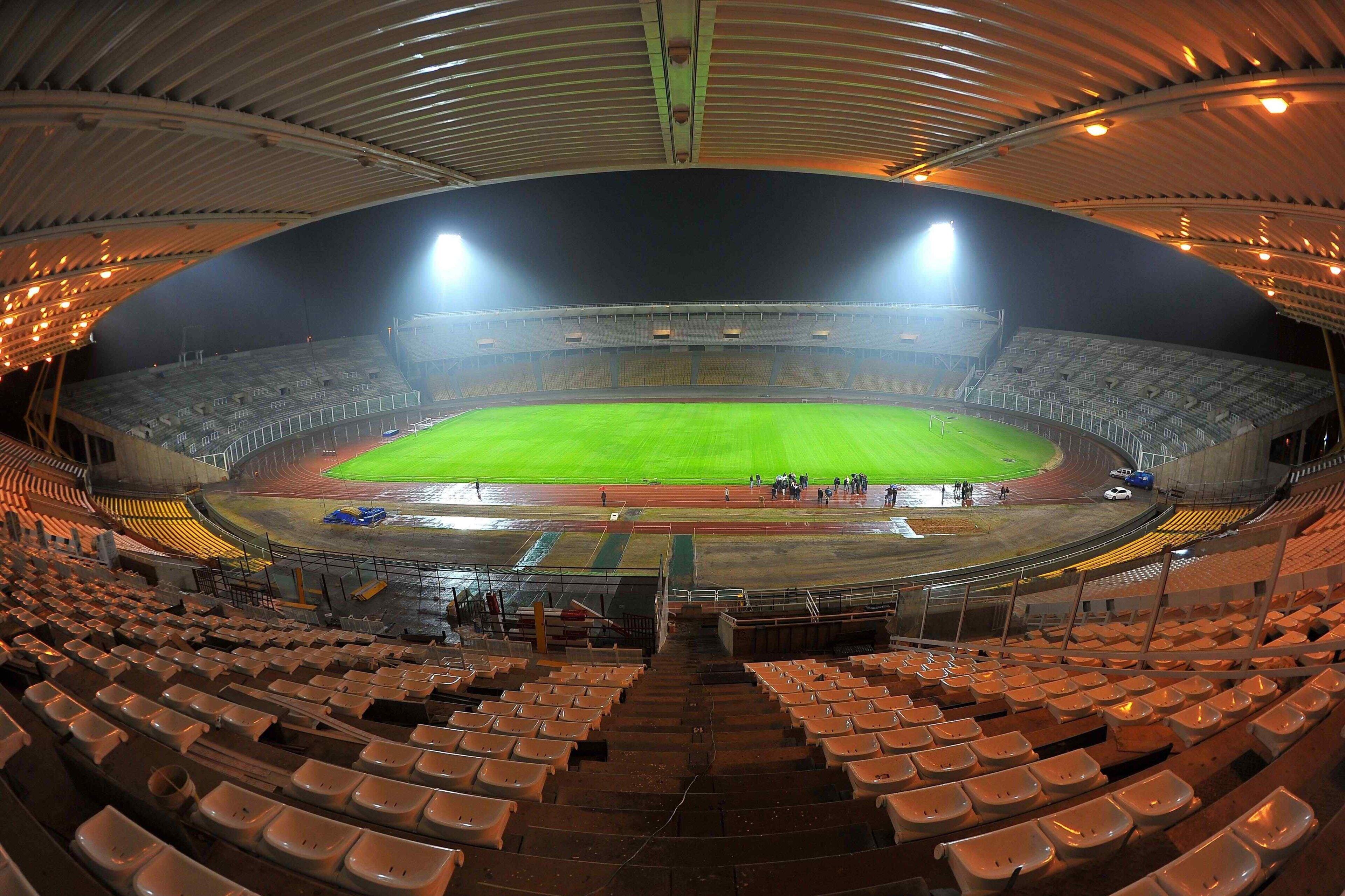 A stadium with multiple tiers of seating, a central field, and a roof structure.