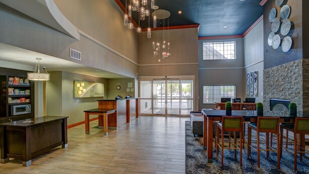 A spacious lobby with a wooden reception desk, a seating area with chairs, a fireplace, and a large window providing natural light. - Holiday Inn Hotel & Suites-Milwaukee Airport by IHG (Milwaukee)