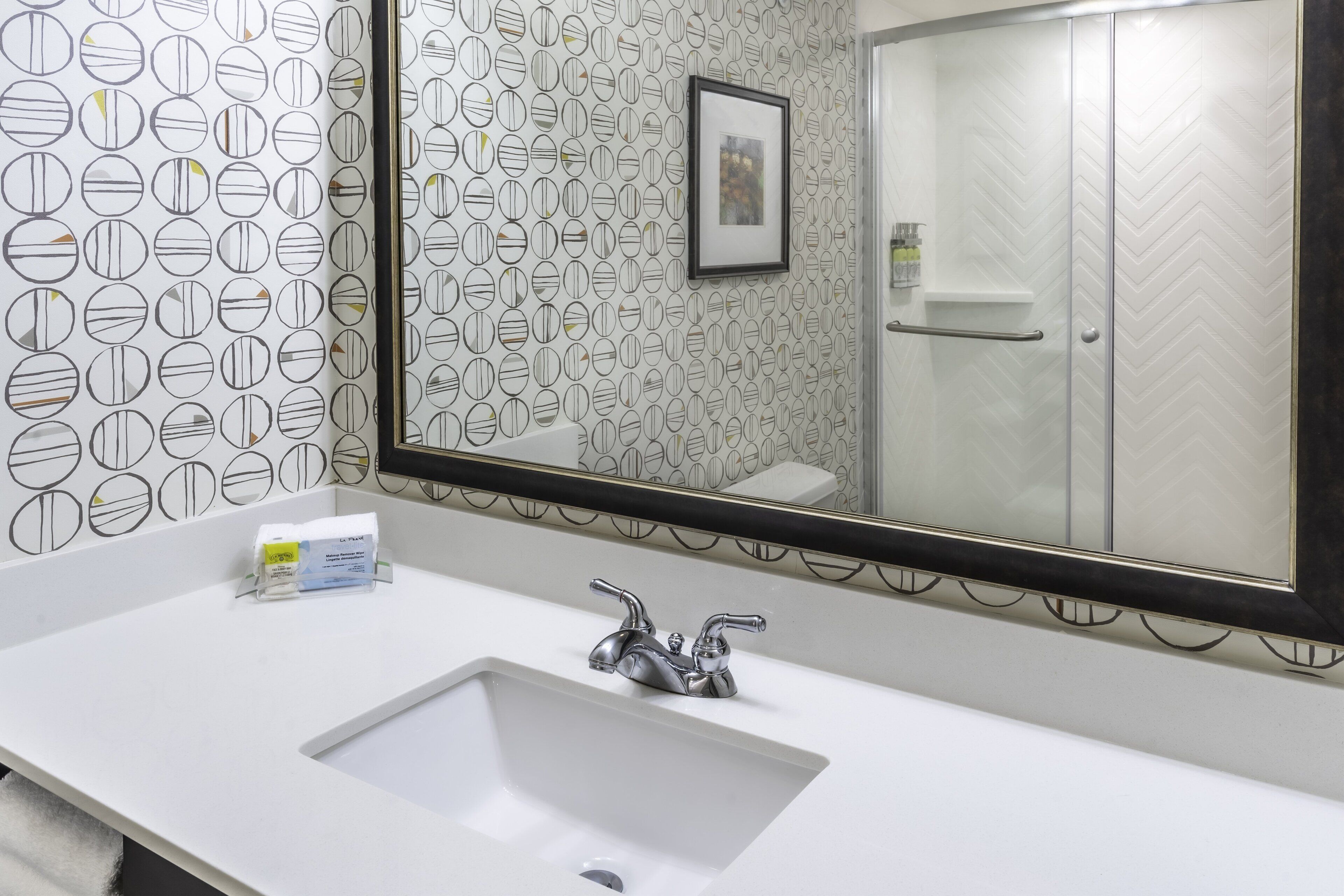 A bathroom with a white sink, a large mirror, and a shower with a herringbone pattern.