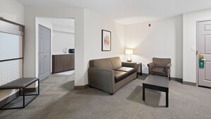 A hotel room with a sofa, a chair, a small table, a lamp, and a door. - Holiday Inn Hotel & Suites-Milwaukee Airport by IHG (Milwaukee)