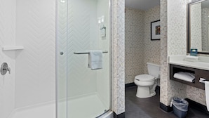 A modern bathroom with a glass-enclosed shower, a white toilet, and a vanity with a mirror. - Holiday Inn Hotel & Suites-Milwaukee Airport by IHG (Milwaukee)