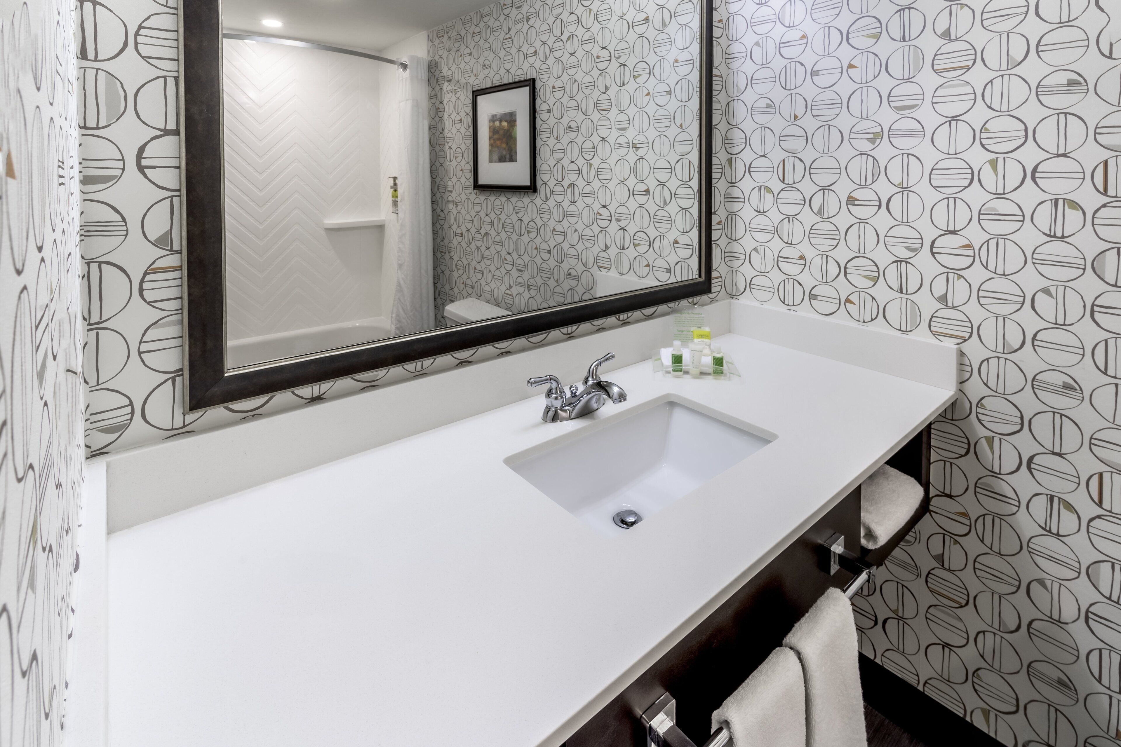 A bathroom with a white sink, a large mirror, and patterned wallpaper.