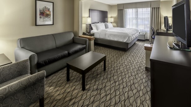 A hotel room with a sofa, a bed, a desk, and a television. - Holiday Inn Hotel & Suites-Milwaukee Airport by IHG (Milwaukee)