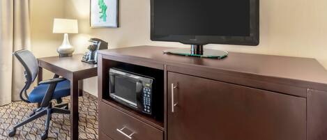 A hotel room with a flat-screen TV, a microwave, a desk with a lamp, and a chair.
