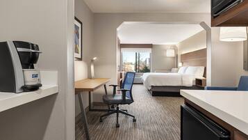 Una habitación de hotel con cama, escritorio, silla, cafetera y televisor.
