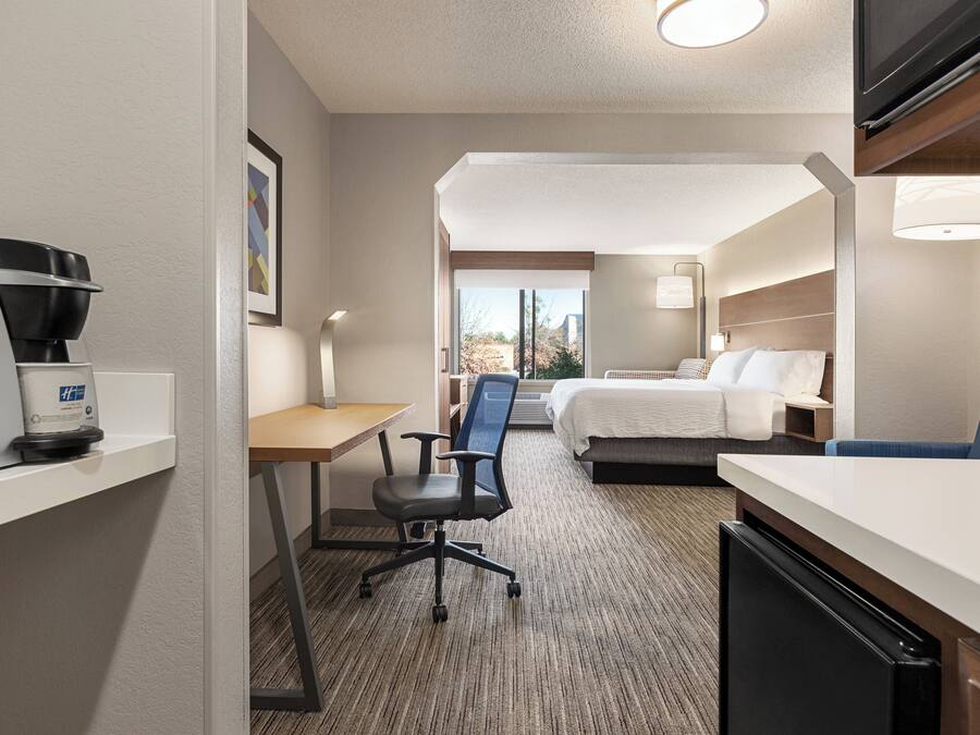 Una habitación de hotel con cama, escritorio, silla, cafetera y televisor.