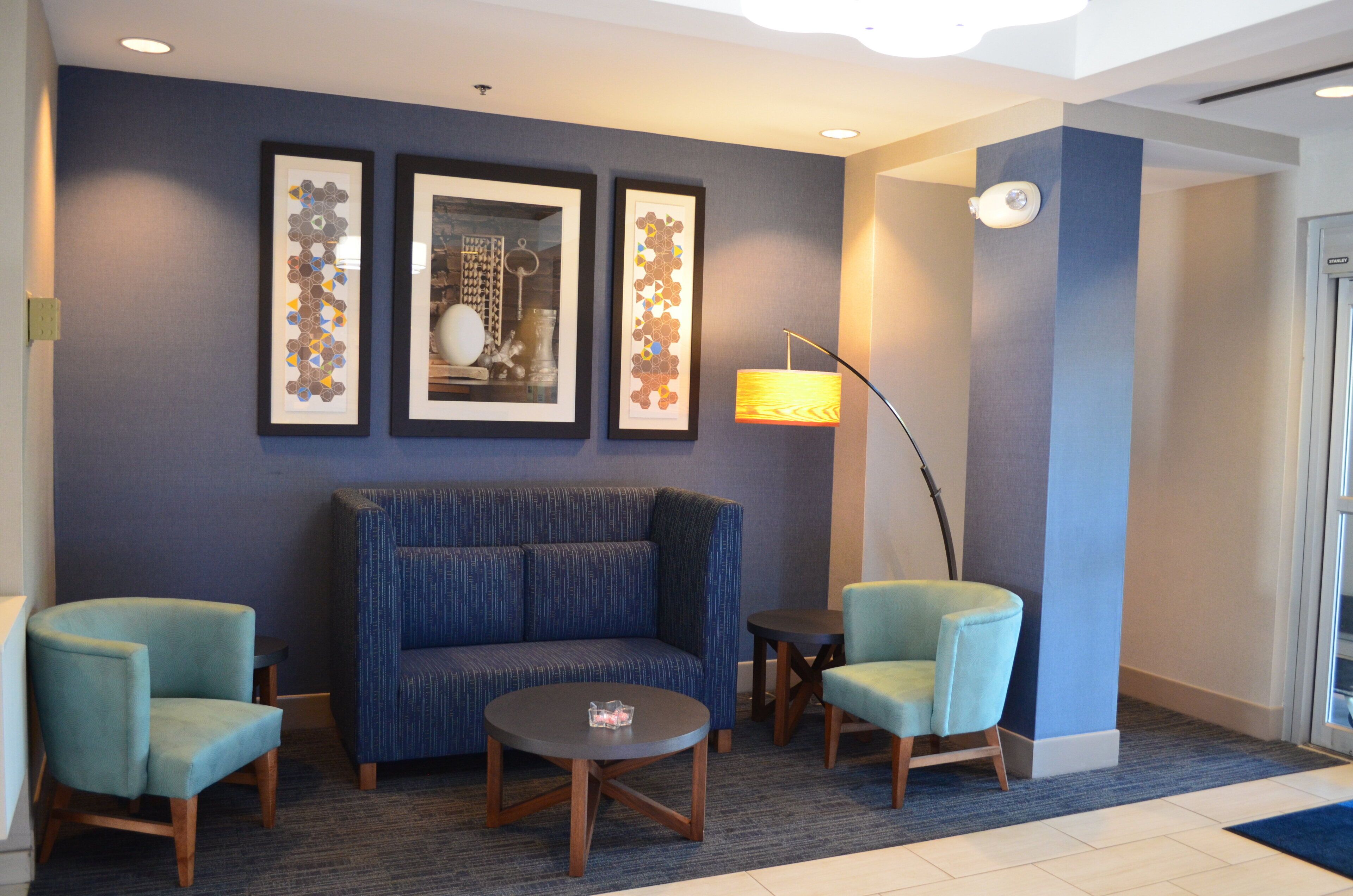 A lobby with a blue sofa, two armchairs, a small table, and three framed artworks on the wall.