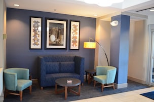 Un hall con un sofá azul, dos sillones, una mesita y tres obras de arte enmarcadas en la pared.