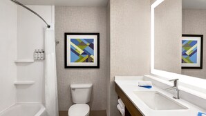 Un baño moderno con bañera, inodoro y lavabo. Hay obras de arte enmarcadas en la pared y artículos de aseo en el estante.