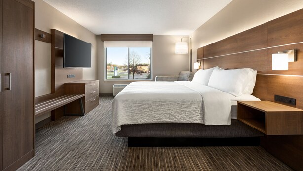 Habitación de hotel con cama, escritorio, televisor de pantalla plana, ventana con vistas y lámpara de pared.