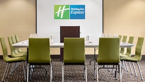 Una sala de conferencias con el logotipo de Holiday Inn Express en la pared, una mesa blanca, sillas verdes y botellas de agua sobre la mesa.