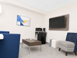 A hotel room with a flat-screen TV, a coffee machine, a microwave, a sofa, a small table, and a decorative wall piece. - Holiday Inn Express Dryden by IHG (Dryden)